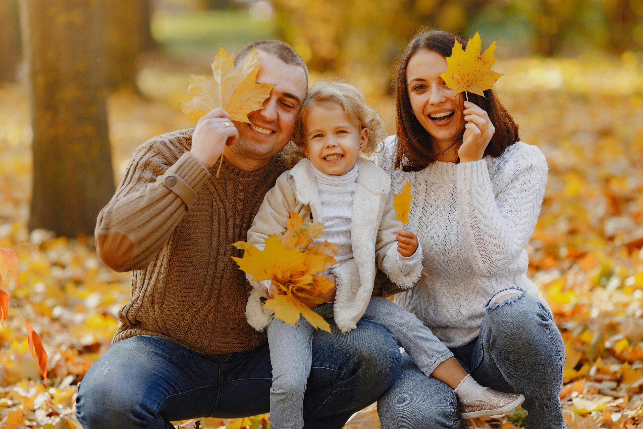 family smiling and playing in autumn leaves after visiting our dentist in Brookhaven, PA